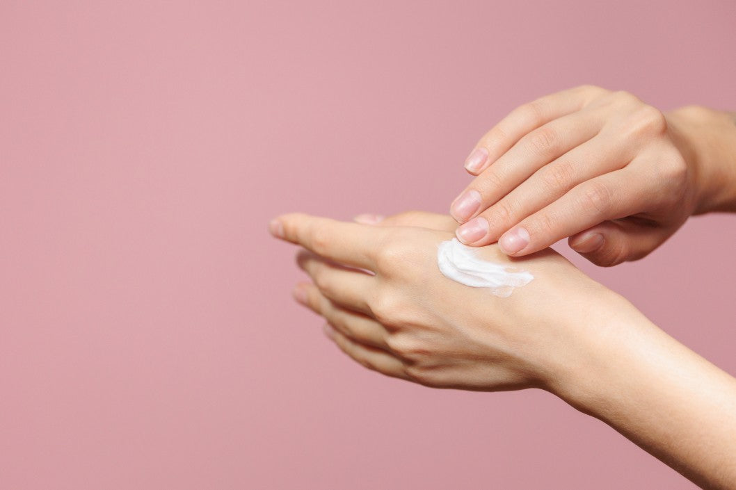women's hands with cream or lotion on a pink background